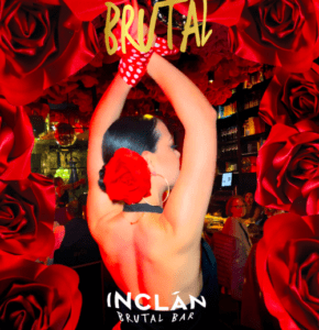 Una bailarina con rosas rojas en el cabello y guantes de lunares, levanta los brazos en un espectáculo cautivador rodeada de flores rojas durante la Cena creativa con espectáculo en Inclán Brutal Bar. - ForTwo - Planes para parejas