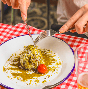 Una persona corta delicadamente un plato decorativo con salsa sabrosa y tomate cherry, sobre un mantel a cuadros, ideal para una cena romántica íntima con auténtica cocina italiana. - ForTwo - Planes para parejas