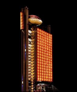 Un edificio futurista con una fachada naranja brillante y una estructura similar a un OVNI contra el cielo nocturno de Barcelona ofrece el escenario perfecto para una "Cena romántica con vistas panorámicas en Barcelona". - ForTwo - Planes para parejas
