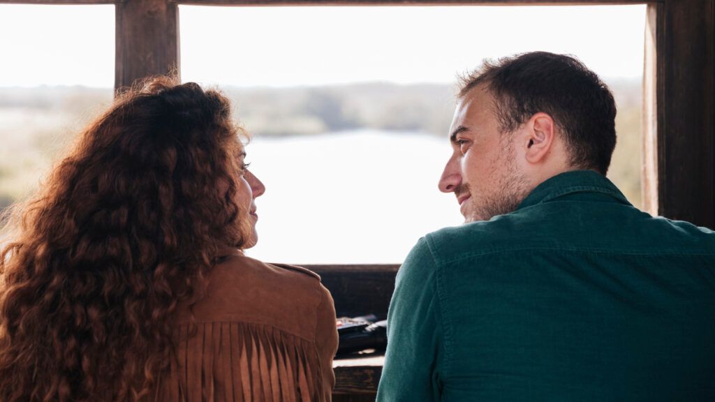 Dos personas se sientan una frente a la otra, enfrascadas en conversaciones profundas, con una vista panorámica del río como telón de fondo. - ForTwo - Planes para parejas