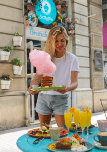 En EatMyTrip Barcelona, una mujer encanta a los amantes de la comida con un desayuno único, que incluye panqueques vibrantes cubiertos con algodón de azúcar en una mesa de cafetería al aire libre en "EatMyTrip Barcelona: Un lugar original para parejas foodies". - ForTwo - Planes para parejas