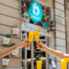 Dos parejas amantes de la comida brindan con mimosas afuera de una encantadora panadería de brunch con decoración floral, que refleja el ambiente vibrante de EatMyTrip Barcelona: Un lugar original para parejas amantes de la comida. - ForTwo - Planes para parejas