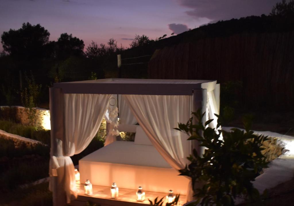 Una cama con dosel suavemente iluminada al aire libre, rodeada de árboles y una valla de madera al anochecer, crea el ambiente perfecto para una escapada romántica cerca de Barcelona. - ForTwo - Planes para parejas