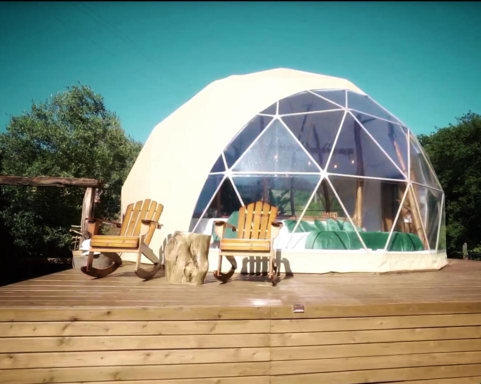 La "Escapada romántica cerca de Barcelona" cuenta con una cúpula geodésica sobre una terraza de madera con dos sillas y una pequeña mesa, rodeada de árboles bajo un cielo despejado, ofreciendo la escapada romántica ideal a las afueras de Barcelona. - ForTwo - Planes para parejas