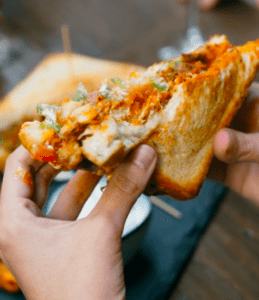 Primer plano de unas manos sosteniendo un sándwich relleno de verduras con salsa, perfecto para un brunch en Lato Café Barcelona: brunch artesanal en Barcelona, encima de una mesa con un bol al fondo. - ForTwo - Planes para parejas