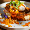 En Lato Café Barcelona, saborea un sándwich gourmet con huevos escalfados, verduras, salsa picante sobre pan crujiente, adornado con flores comestibles y nueces para una experiencia de brunch artesanal perfecta. - ForTwo - Planes para parejas