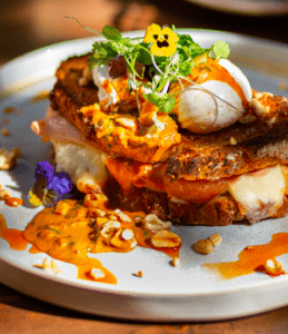 En Lato Café Barcelona, saborea un sándwich gourmet con huevos escalfados, verduras, salsa picante sobre pan crujiente, adornado con flores comestibles y nueces para una experiencia de brunch artesanal perfecta. - ForTwo - Planes para parejas