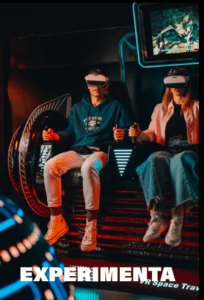 En el Museo del Videojuego de Madrid, dos personas se sumergen en un emocionante simulador de movimiento usando gafas de realidad virtual, con "EXPERIMENTA" mostrado debajo. - ForTwo - Planes para parejas