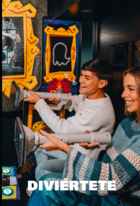 Dos personas sonríen y juegan a un juego de disparos arcade, capturando el espíritu vibrante del Museo del Videojuego de Madrid, con el texto DIVIÉRTETE debajo. - ForTwo - Planes para parejas