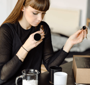 En Barcelona, una mujer huele atentamente aceites esenciales, rodeada de ingredientes y una caja marrón para el Taller de velas de soja en Barcelona, preparándose para crear hermosas velas de soja en un entorno sereno. - ForTwo - Planes para parejas