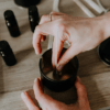 Una persona elabora cera utilizando el kit del Taller de velas de soja en Barcelona, revolviendo suavemente la cera derretida mientras las botellas de aceite esencial se esparcen sobre la mesa, capturando el encanto del taller. - ForTwo - Planes para parejas