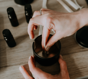 Una persona elabora cera utilizando el kit del Taller de velas de soja en Barcelona, revolviendo suavemente la cera derretida mientras las botellas de aceite esencial se esparcen sobre la mesa, capturando el encanto del taller. - ForTwo - Planes para parejas