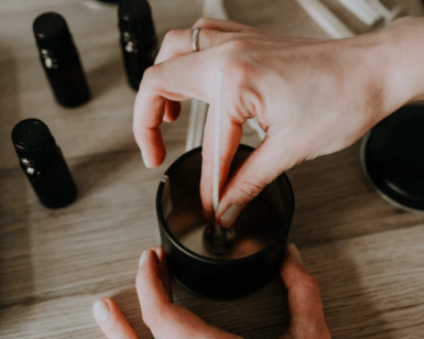 Una persona elabora cera utilizando el kit del Taller de velas de soja en Barcelona, revolviendo suavemente la cera derretida mientras las botellas de aceite esencial se esparcen sobre la mesa, capturando el encanto del taller. - ForTwo - Planes para parejas
