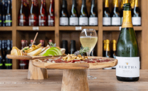 La Terraza entre viñedos en el Penedès evoca un ambiente encantador con vinos y embutidos en soportes de madera, perfectos para disfrutar bajo la luz del sol. Las botellas en los estantes crean una atmósfera encantadora que evoca viñedos lejanos. - ForTwo - Planes para parejas