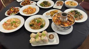 Una mesa en Thai Oasiz está repleta de rollitos de primavera, tazones de fideos, estofado y brochetas en elegantes platos blancos. Disfruta de Thai Oasiz: Un viaje gastronómico a Tailandia y saborea cada bocado. - ForTwo - Planes para parejas