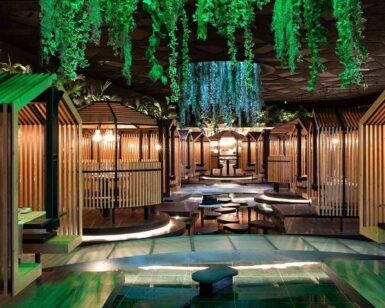 Un interior de restaurante moderno con cabinas de madera, vegetación colgante e iluminación ambiental crea una atmósfera serena similar a Thai Oasiz: Un viaje gastronómico a Tailandia. - ForTwo - Planes para parejas