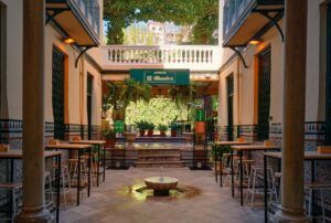 Esta cafetería con patio de Granada es un oasis con mesas y sillas, rodeado de exuberantes plantas y paredes de azulejos bajo el cartel que dice Jardín Alhambra. - ForTwo - Planes para parejas